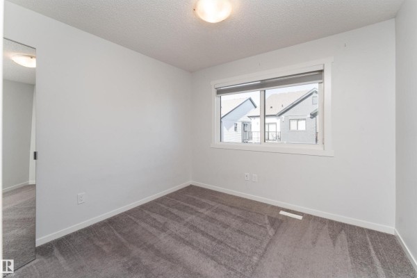 Empty bedroom with grey carpet, white walls, and a window overlooking houses. - #40 850 Secord Bv Nw, Edmonton