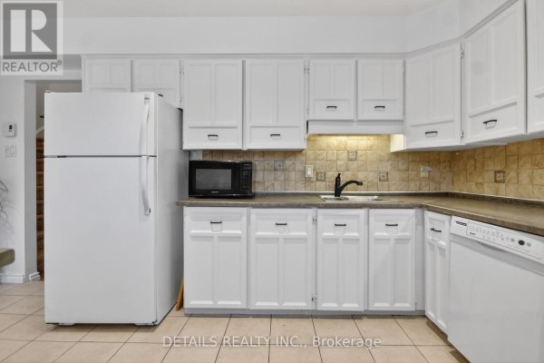 White kitchen cabinets with dark hardware, beige tiled backsplash, and appliances. - 40 Appleby Private, Ottawa