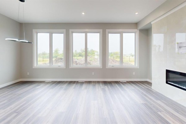 Living room with light gray walls, three large windows, and a modern fireplace with marble surround. - 40 Bremner Drive, Headingley