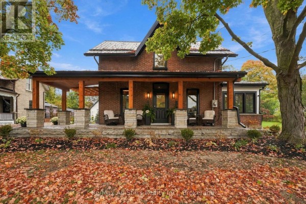 Front view of a red brick house with a long, covered porch and stone pillars. - 40 Caroline Street, Kawartha Lakes