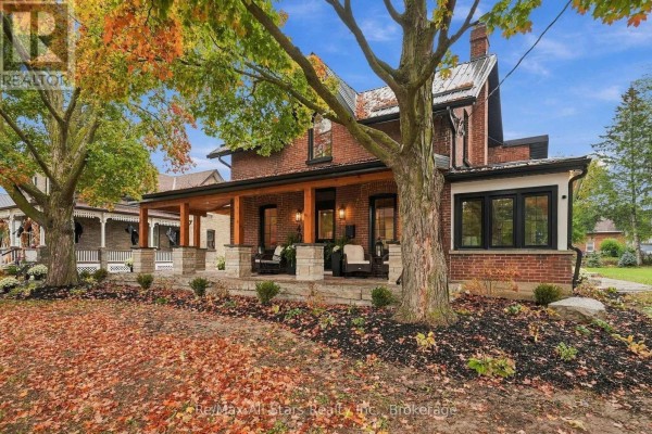 Side view of the brick house showing the porch, large tree, and fall leaves. - 40 Caroline Street, Kawartha Lakes