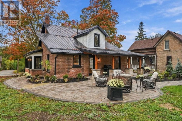 Rear view of the house with a stone patio, wicker furniture, and landscaping. - 40 Caroline Street, Kawartha Lakes