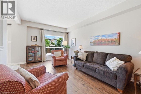 Living room with a large window, sofa, armchairs, and dark wood flooring. - 40 Dartmouth Gate Unit# 10, Stoney Creek