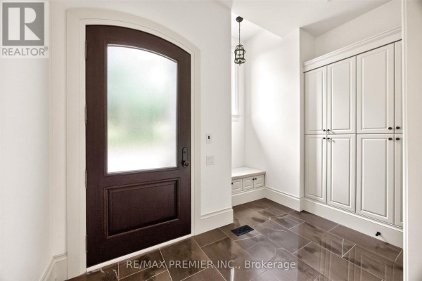 Arched dark wood door, storage bench, and cabinets in entryway - 40 Golf Avenue Vaughan