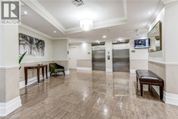 Building lobby with polished stone floors, elevators, a chandelier, and a dark green armchair with a side table. - 40 Harding Boulevard Unit# 603, York