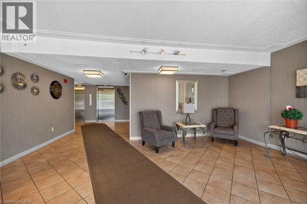 Apartment building lobby with grey textured walls, tiled floors, and elevators. - 40 Harrisford Street Unit# 103, Hamilton