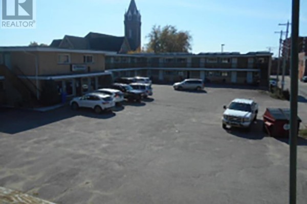 Aerial view of a multi-family building with a parking lot, parked vehicles, and a brick church steeple in the background. - 40 Hynes St, Sault Ste  Marie