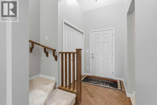 Entrance hallway with light gray walls, beige carpeted stairs, and wooden banister. - 40 Panatella Mews Nw, Calgary