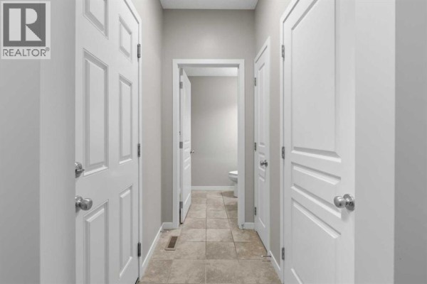 Hallway with beige tiled floor, white doors, and an open doorway to a toilet. - 40 Panatella Mews Nw, Calgary