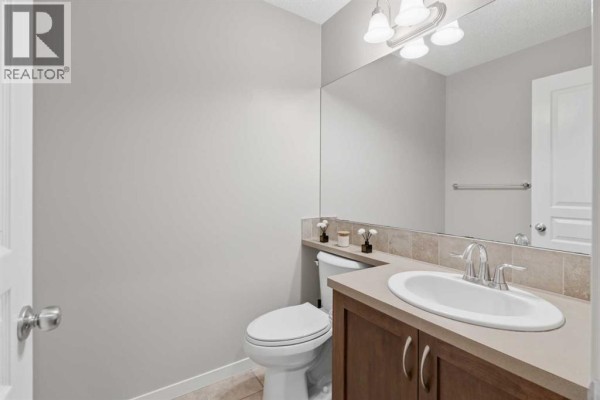 Powder room with beige tiled floor, white toilet, wooden vanity, and large mirror. - 40 Panatella Mews Nw, Calgary