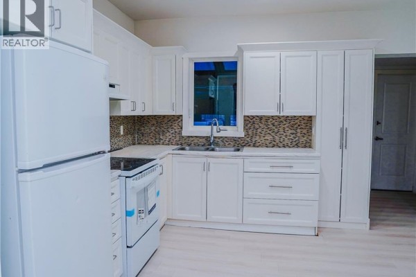 White L-shaped kitchen with white cabinets, stainless steel sink, and a window above the sink. - 40 Park Hill Road, Cambridge