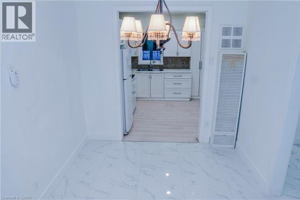 View through an open doorway into a white kitchen with stainless steel appliances and tile flooring. - 40 Park Hill Road, Cambridge