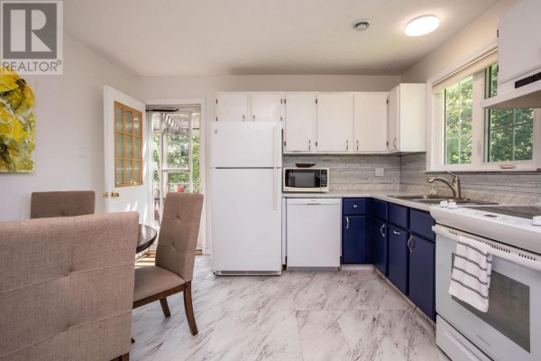 Kitchen with white cabinets, blue lower cabinets, white appliances, light marble-look flooring, and dining area. - 40 Poplar Drive, Cornwall