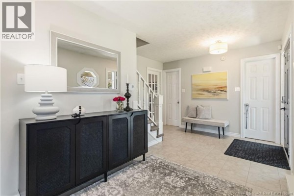 Foyer with beige tiled floor, dark console table, mirror, bench, and access to staircase and rooms. - 40 Tamarack Terrace, Moncton