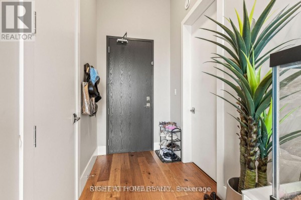 Apartment entrance foyer with wood flooring, a dark wood door, shoe rack, and a large potted plant. - 400 - 1705 Fiddlehead Place, London North