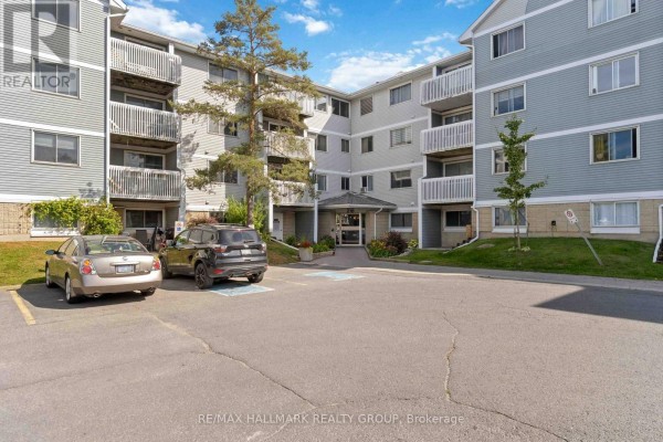 Front entrance of an apartment building with cars parked in the lot and landscaping. - 400 - 218 Viewmount Drive, Ottawa