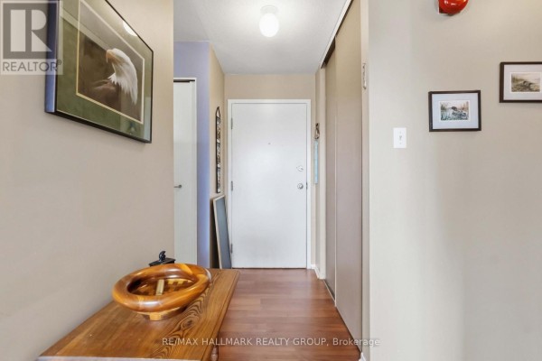 Interior view of an apartment entrance with wood flooring, a wooden console table, and white doors. - 400 - 218 Viewmount Drive, Ottawa
