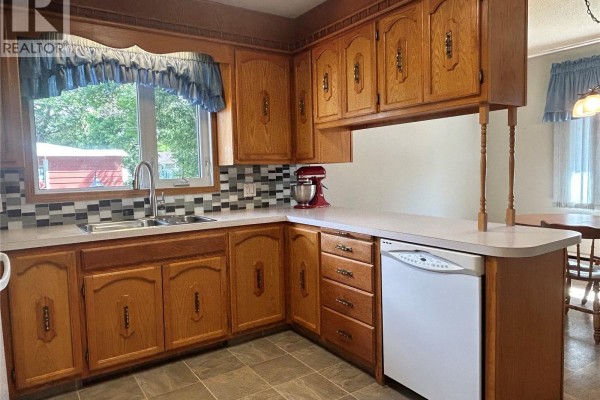 Corner kitchen with oak cabinets, tiled backsplash, white countertop, and dishwasher. - 400 Gallaway Street, Estevan