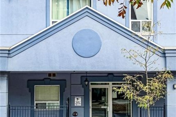 Close-up of the apartment building entrance with a peaked roof, light blue facade, and glass doors. - 400 York Boulevard Unit# 407, Hamilton