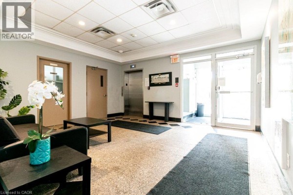 Apartment building lobby with a terrazzo floor, elevators, black furniture, and potted plants. - 400 York Boulevard Unit# 407, Hamilton