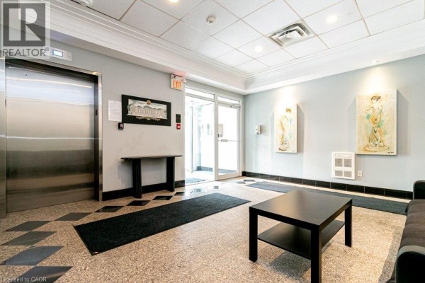 Apartment building lobby featuring a terrazzo floor, elevators, black tables, and framed artwork on walls. - 400 York Boulevard Unit# 407, Hamilton