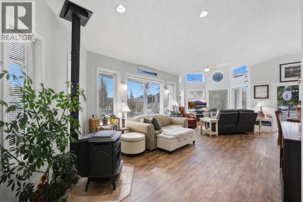 Spacious living room with a wood-burning stove, large windows, and multiple seating areas. - 4001, 35468 Range Road 30, Rural Red Deer County