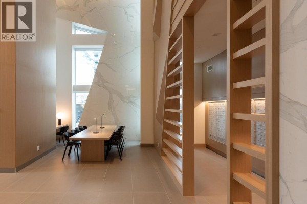 Building lobby with a long wooden table, chairs, marble accent wall, and mailboxes. - 4002 680 Quayside Drive, New Westminster