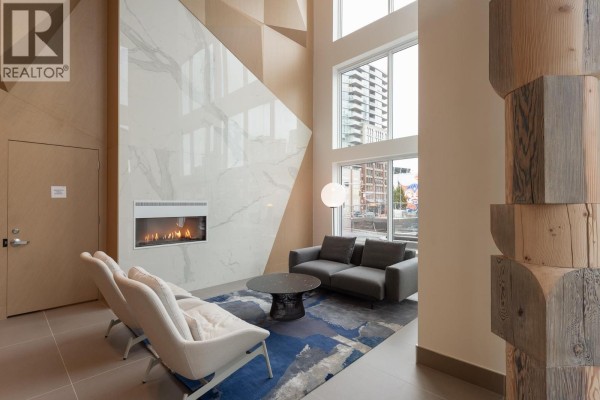Apartment building lounge area with a fireplace, grey sofas, chairs, and a blue rug. - 4002 680 Quayside Drive, New Westminster