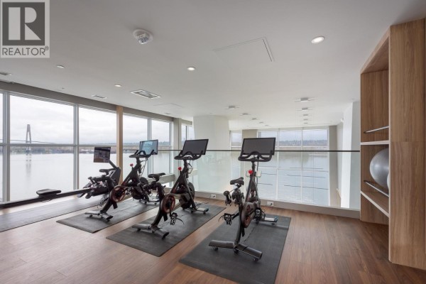Indoor cycling room with stationary bikes, rowing machine, and water views from windows. - 4002 680 Quayside Drive, New Westminster