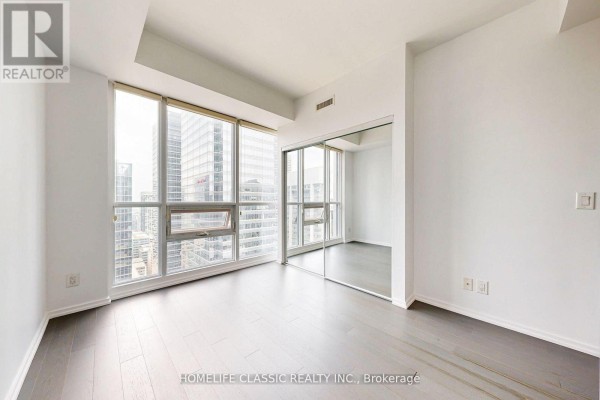 Empty bedroom with large windows, mirrored closet doors, and dark wood flooring. - 4006 - 70 Temperance Street, Toronto