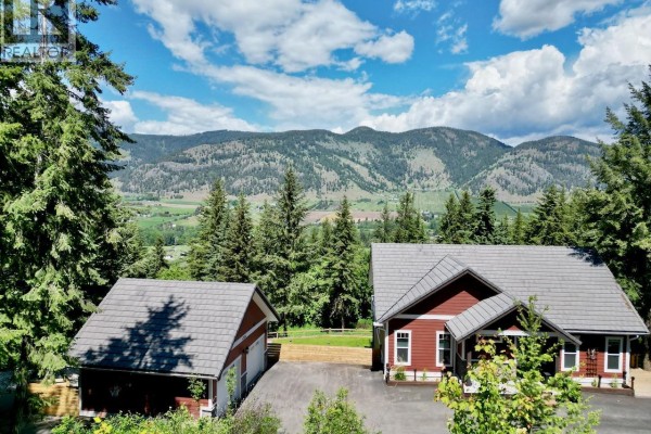 Aerial view of a red house and garage with mountainous backdrop. - 4006 Coachwood Close, Coldstream