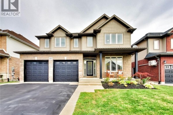 Close-up of the front entrance of a beige and brick two-story house with dark grey garage doors. - 4007 Bush Crescent, Beamsville
