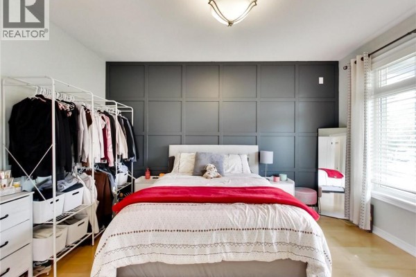 Bedroom with a king-size bed, dark grey paneled accent wall, and a clothing rack. - 4007 Bush Crescent, Beamsville