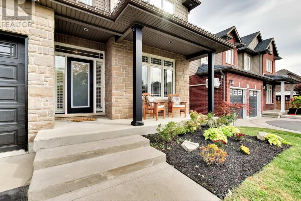 Close-up of the covered front porch with stone pillars, seating, and landscaping. - 4007 Bush Crescent, Lincoln