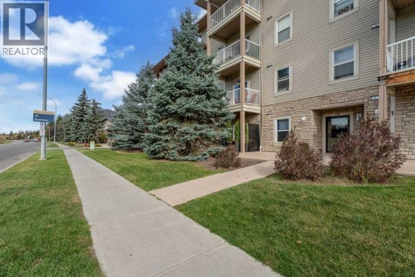 Sidewalk leading to an apartment building entrance with green trees and grass. - 401, 174 N Railway Street, Okotoks