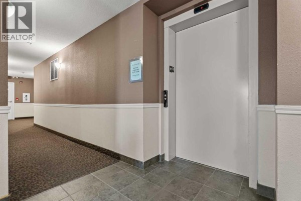 Interior hallway of an apartment building with tiled flooring and an elevator. - 401, 174 N Railway Street, Okotoks
