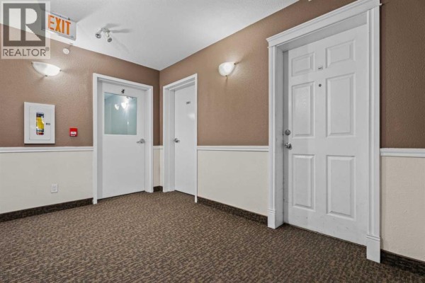 Interior apartment building hallway with carpet, doors, and an exit sign. - 401, 174 N Railway Street, Okotoks