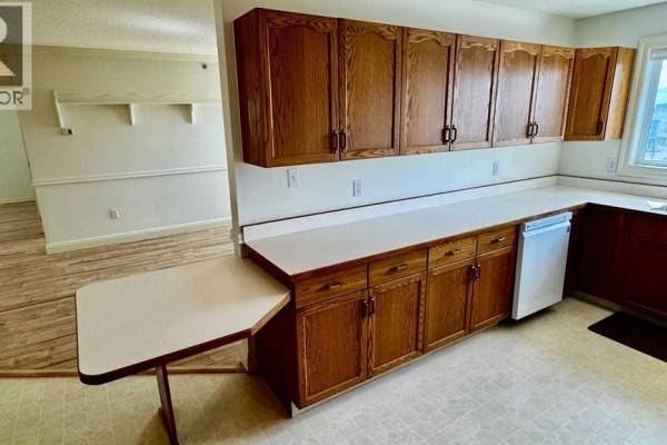 Kitchen with white countertops, oak cabinets, dishwasher, and an attached table. - 401, 9919 99 Avenue, Grande Prairie