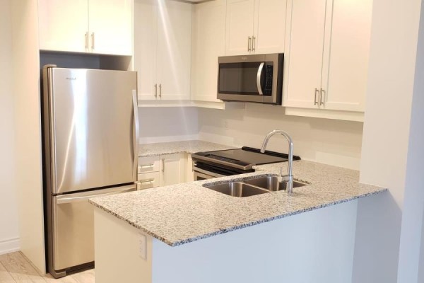 Kitchen with stainless steel refrigerator, microwave, and oven, plus granite countertops and white cabinetry. - 401 - 1050 Main Street, Milton