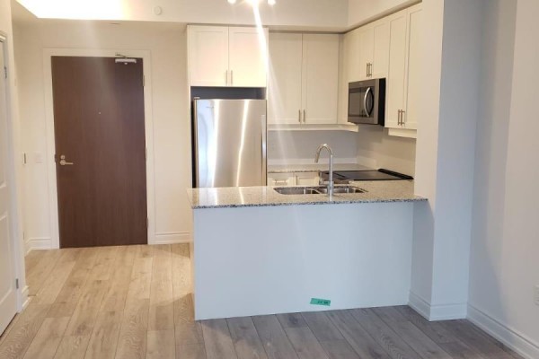 Open concept apartment interior showing a kitchen area and a living space with light wood flooring. - 401 - 1050 Main Street, Milton