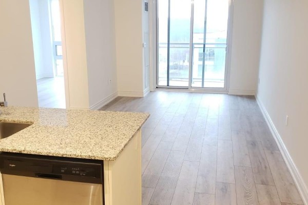 Spacious living area with light gray wood flooring and sliding glass doors leading to a balcony. - 401 - 1050 Main Street, Milton
