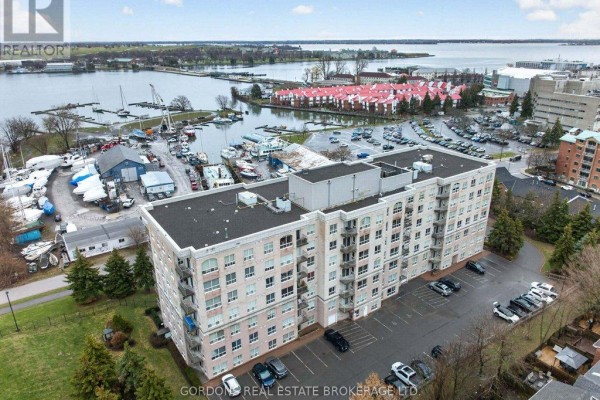 Aerial view of a cream-colored brick apartment building complex with a marina and city skyline. - 401 - 350 Wellington Street, Kingston