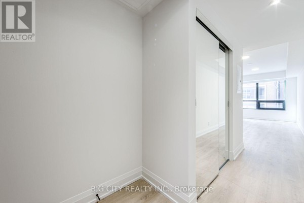 Hallway with white walls, light wood floors, and a mirrored sliding closet door. - 401 - 36 Brentcliffe Road, Toronto