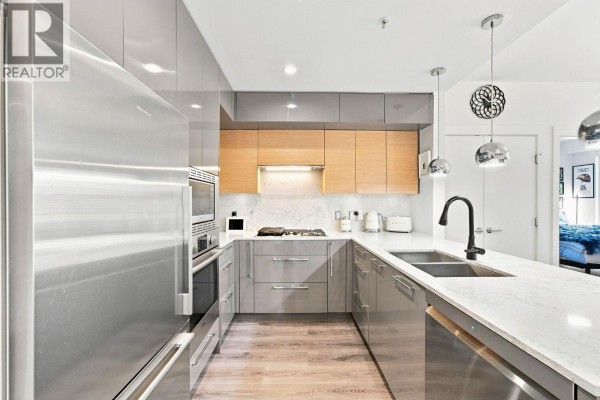 U-shaped kitchen with stainless steel appliances, grey and wood cabinetry, and a large island with sink. - 401 1327 Draycott Road, North Vancouver