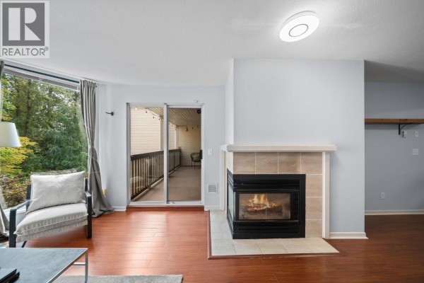 Living room fireplace with tiled surround, view of sliding glass door to balcony. - 401 22233 River Road, Maple Ridge