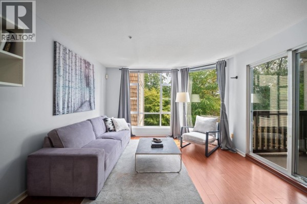 Living room with purple sectional sofa, coffee table, armchair, fireplace and large windows. - 401 22233 River Road, Maple Ridge