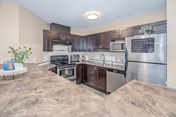 Kitchen corner showing stove, dishwasher, sink, stainless steel refrigerator, and dark cabinets. - 401 33738 King Road Road, Abbotsford