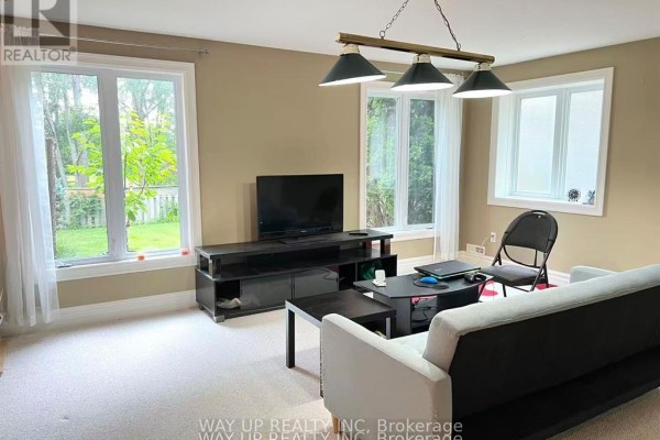 Living area with beige carpet, sofa, coffee table, and multiple windows. - 401 Kingbird Court, London North