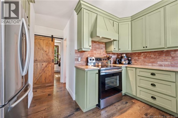 Corner kitchen with light green cabinets, stainless steel stove, and brick backsplash. - 401 Montgomery Avenue, Riverview