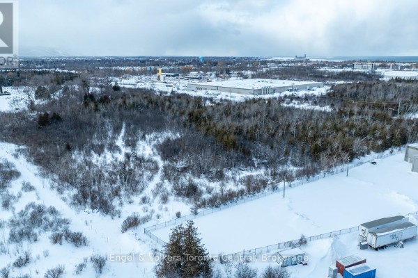 Winter aerial view of a large treed lot with snow, fencing, and industrial buildings nearby. - 401 Raglan Street, Collingwood